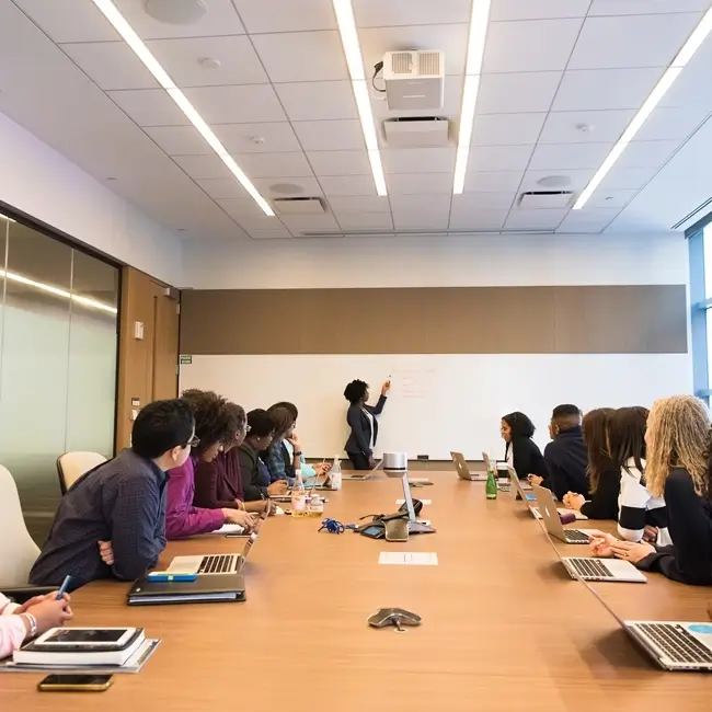 A group of people in a meeting in a boardroom watching a person present.